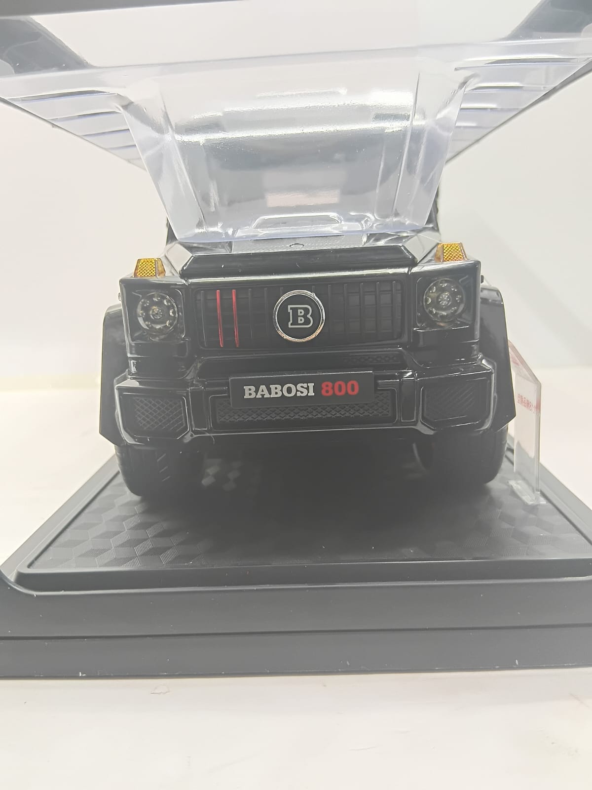 A black diecast model car of a luxury SUV with the hood open, featuring a front grille with a circular 'B' emblem and a front plate reading 'BABOSI 800', displayed on a black base.
